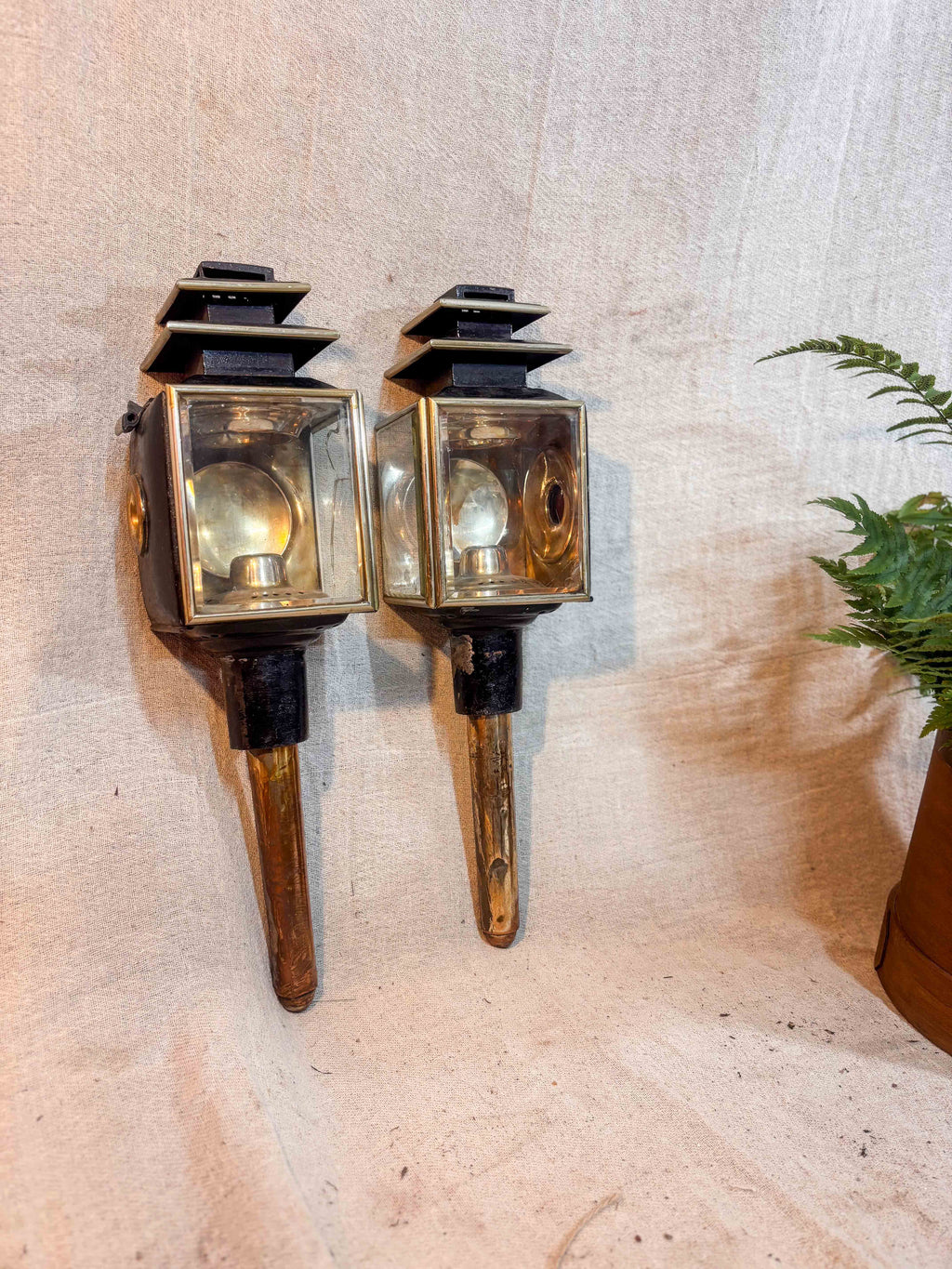 Pair of antique carriage lamps with glass panels on a textured wall.