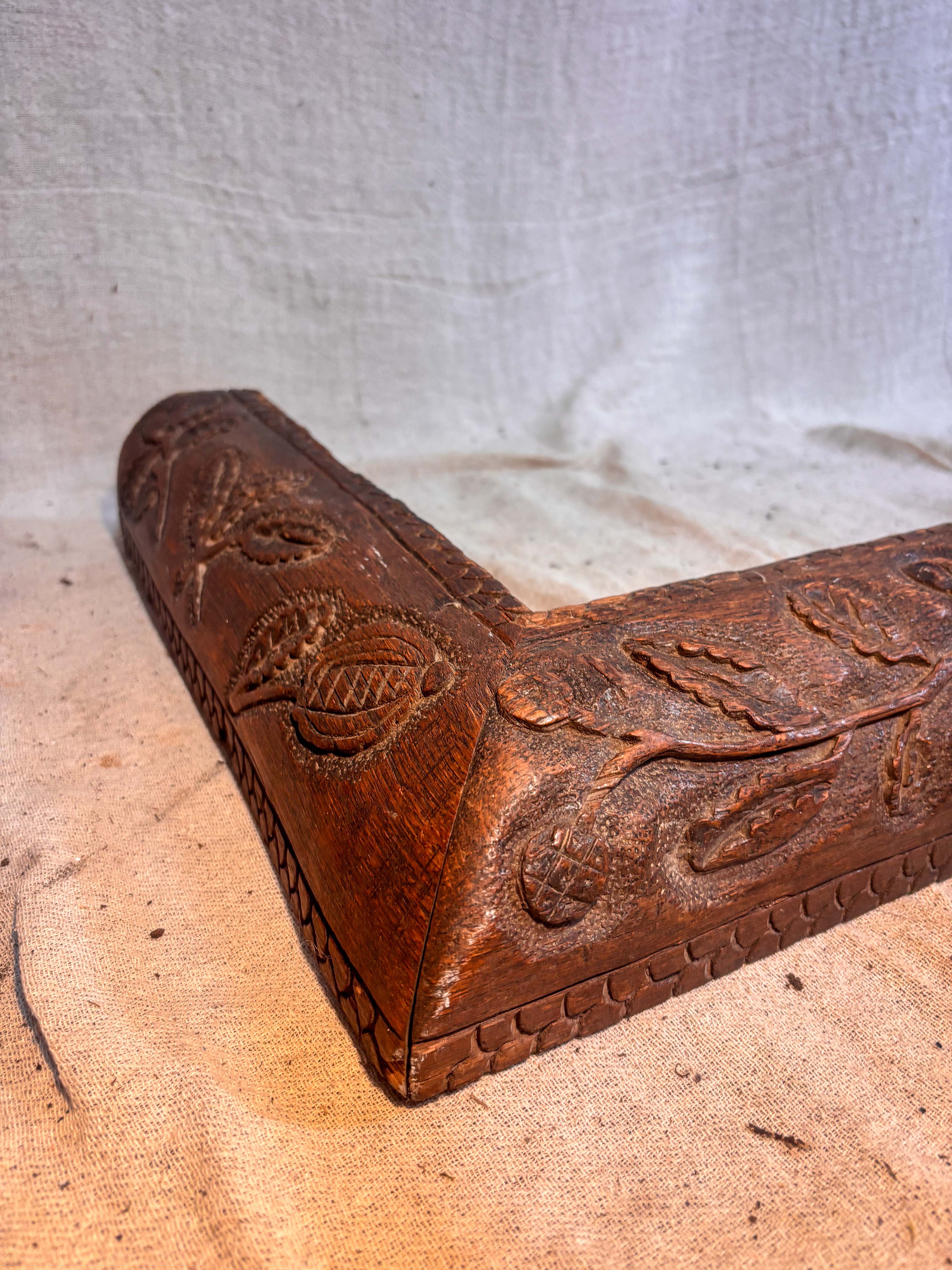 Decorative wooden fire fender corner with intricate carvings on a textured surface.