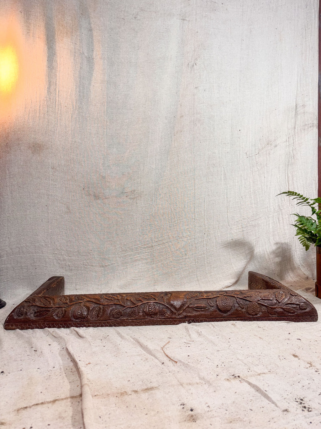 Decorative wooden fire fender with intricate carvings on a textured white wall.