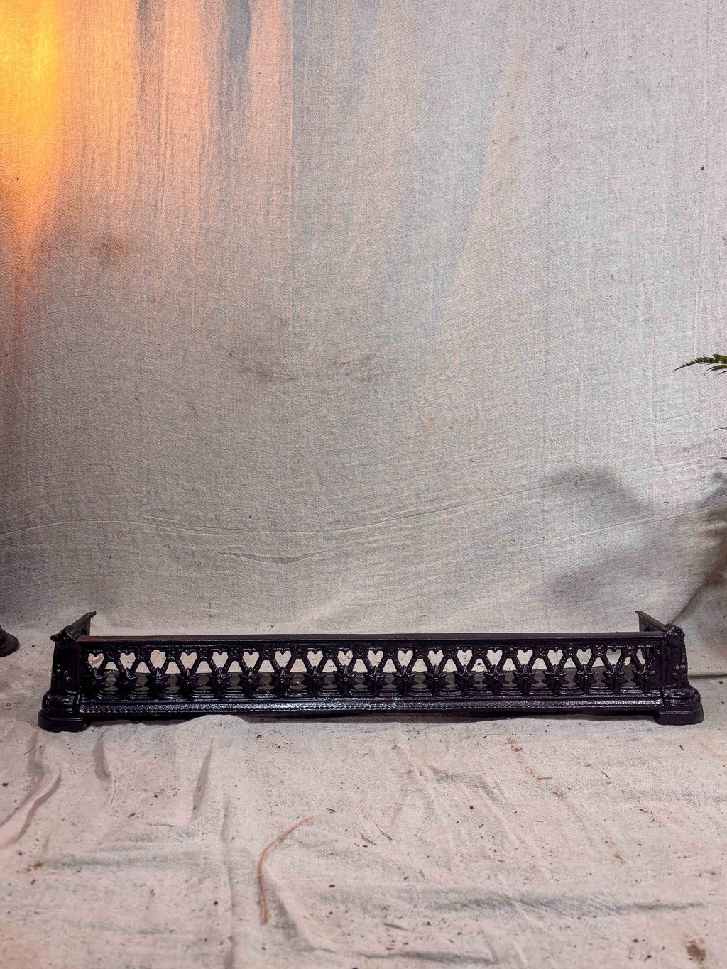 Decorative metal fireplace fender with intricate designs on a textured white surface.