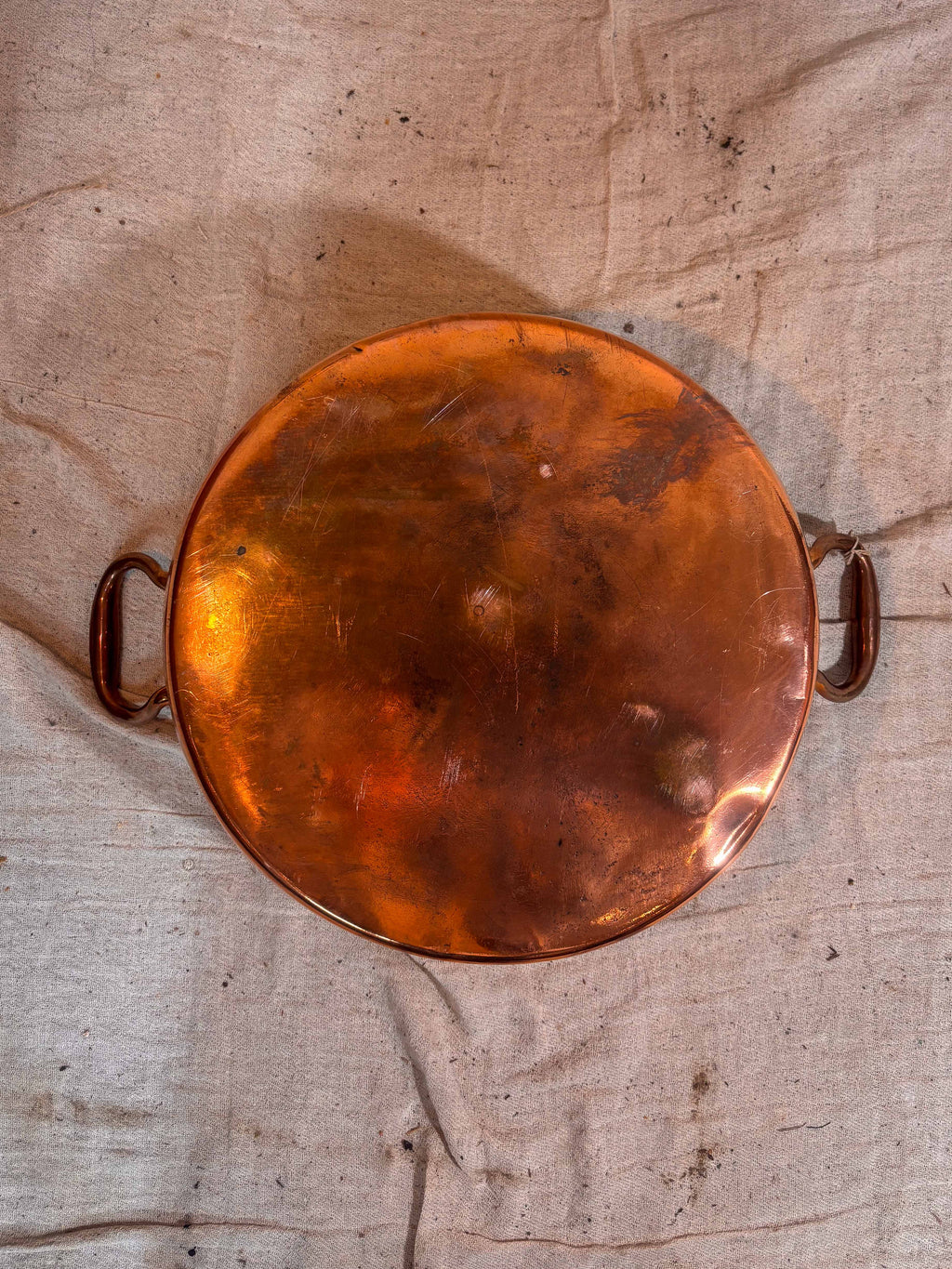 Base of a Copper pan with handles on a textured beige surface
