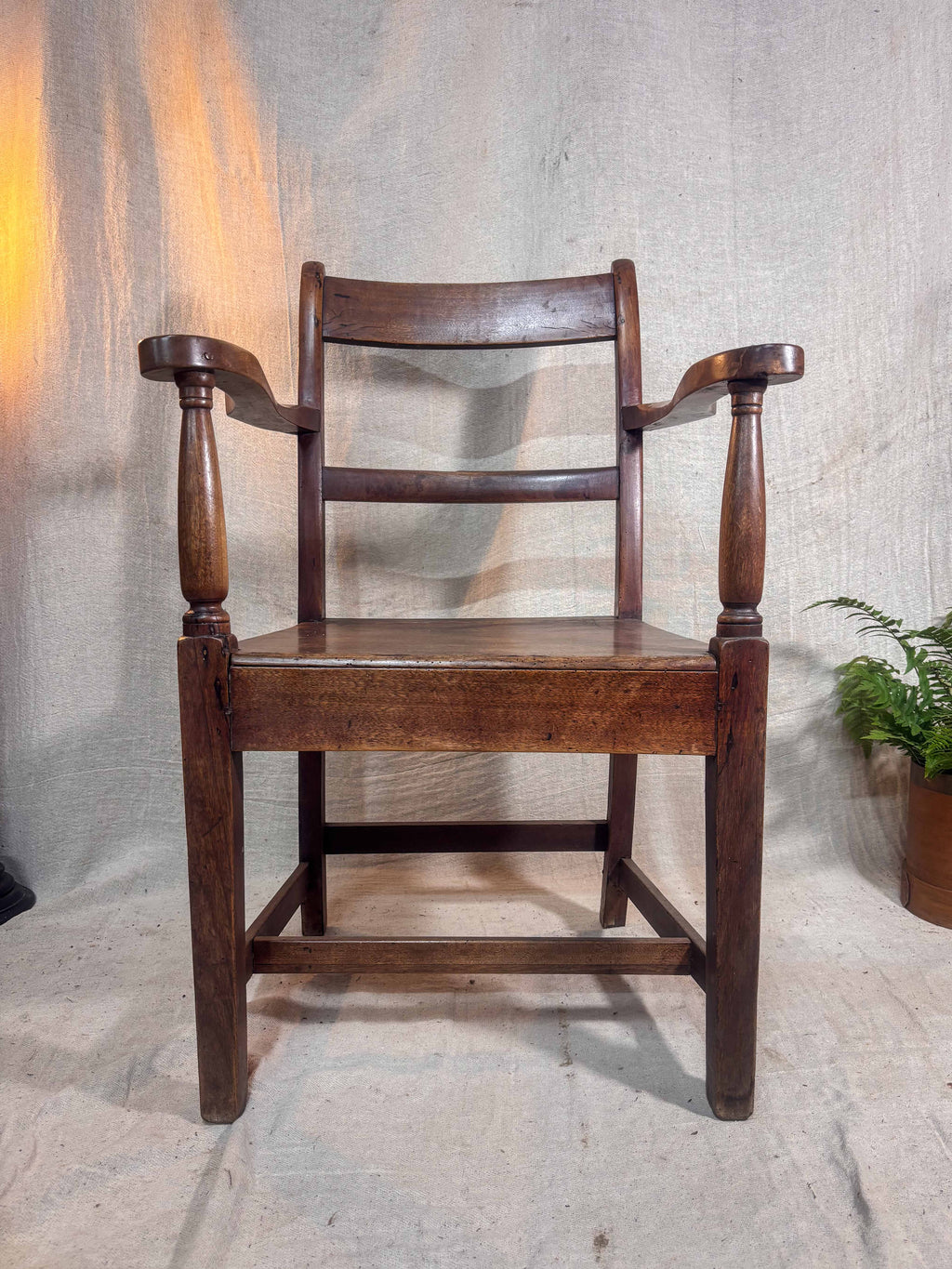 Wooden chair with armrests against a textured wall.
