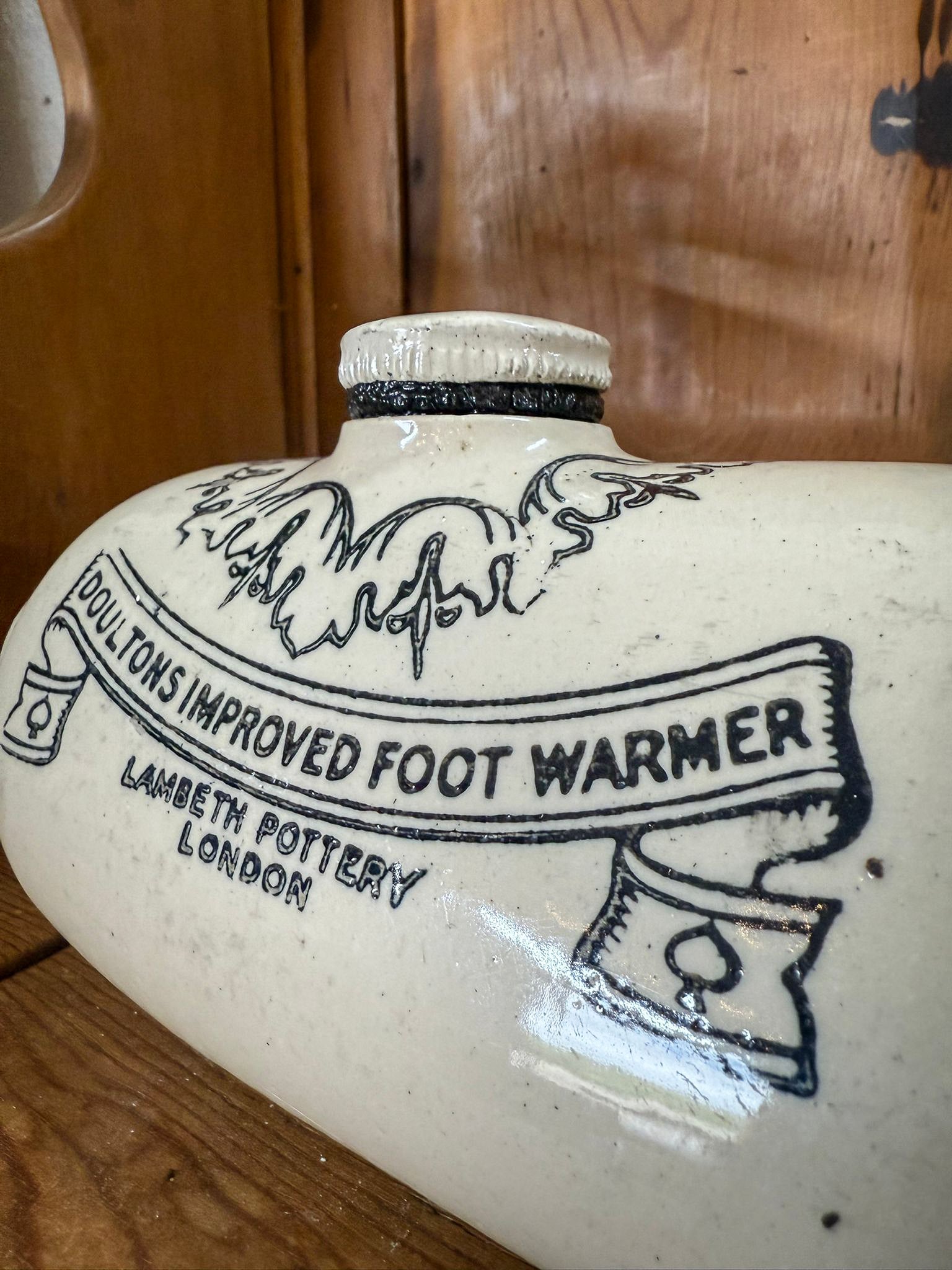 Ceramic foot warmer with 'Doultons Improved Foot Warmer' branding on a wooden surface