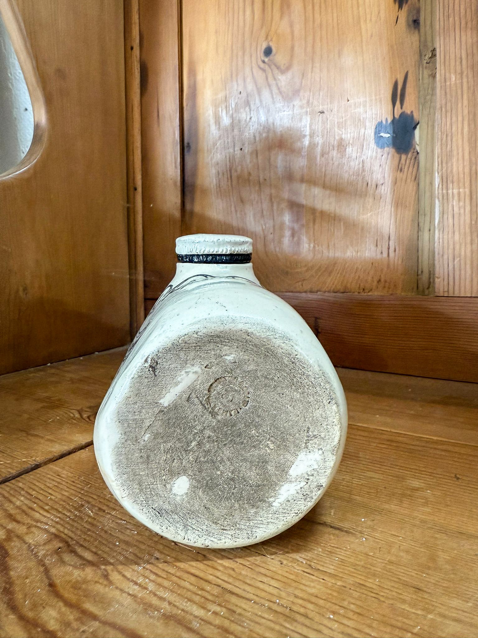 Vintage ceramic bottle on a wooden surface with a wooden cabinet in the background