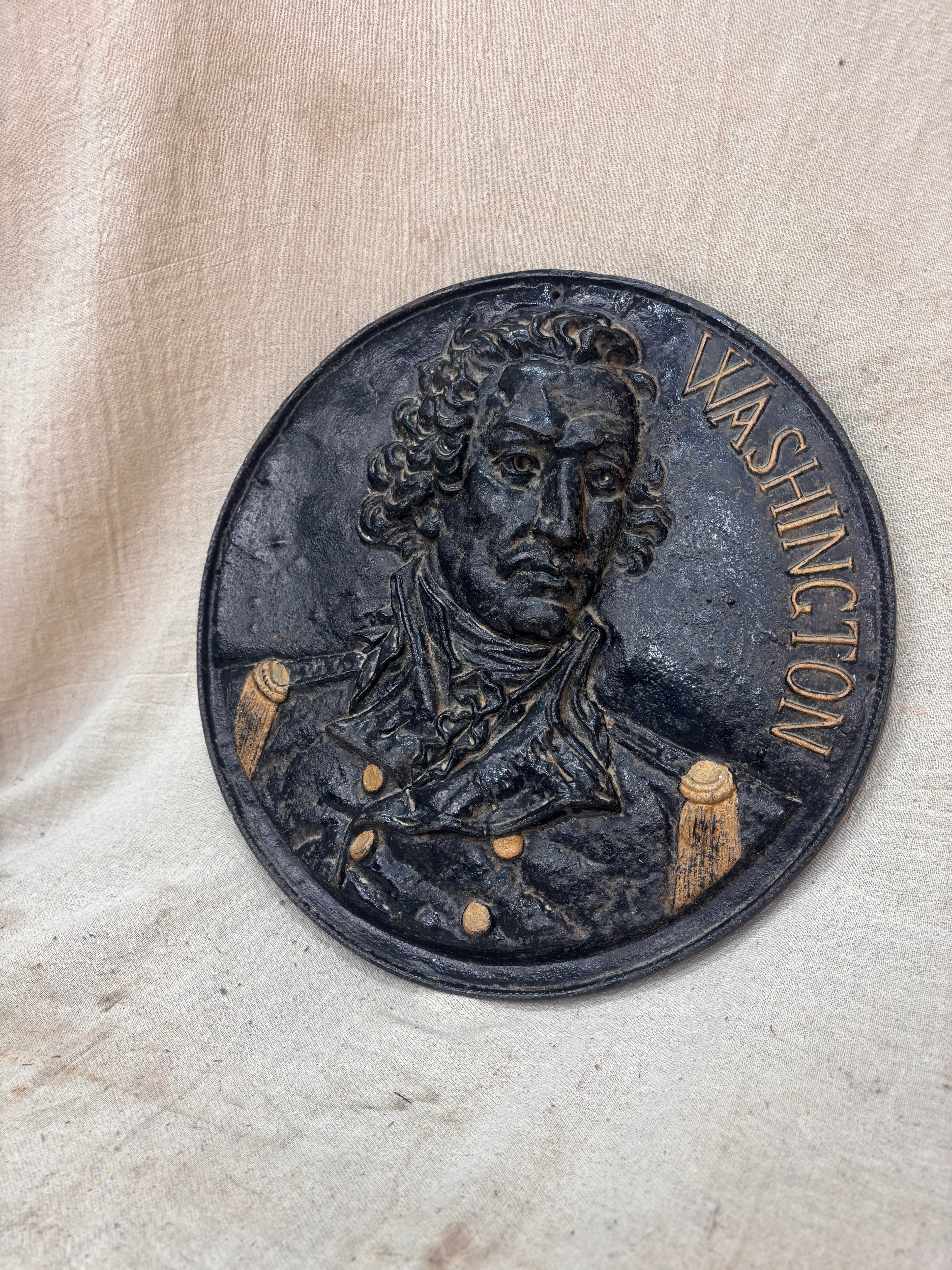 Metal plaque with a portrait of a historical figure and 'Washington' text on a beige fabric background