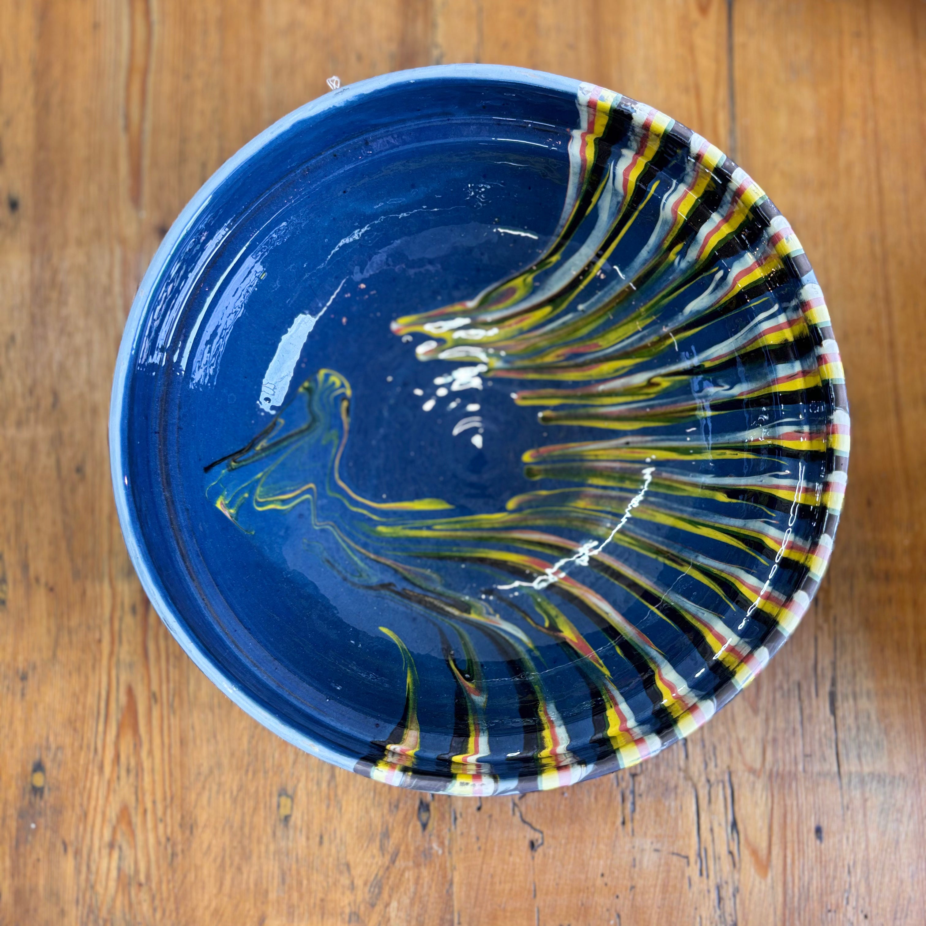 Blue ceramic bowl with abstract yellow and red design on a wooden surface