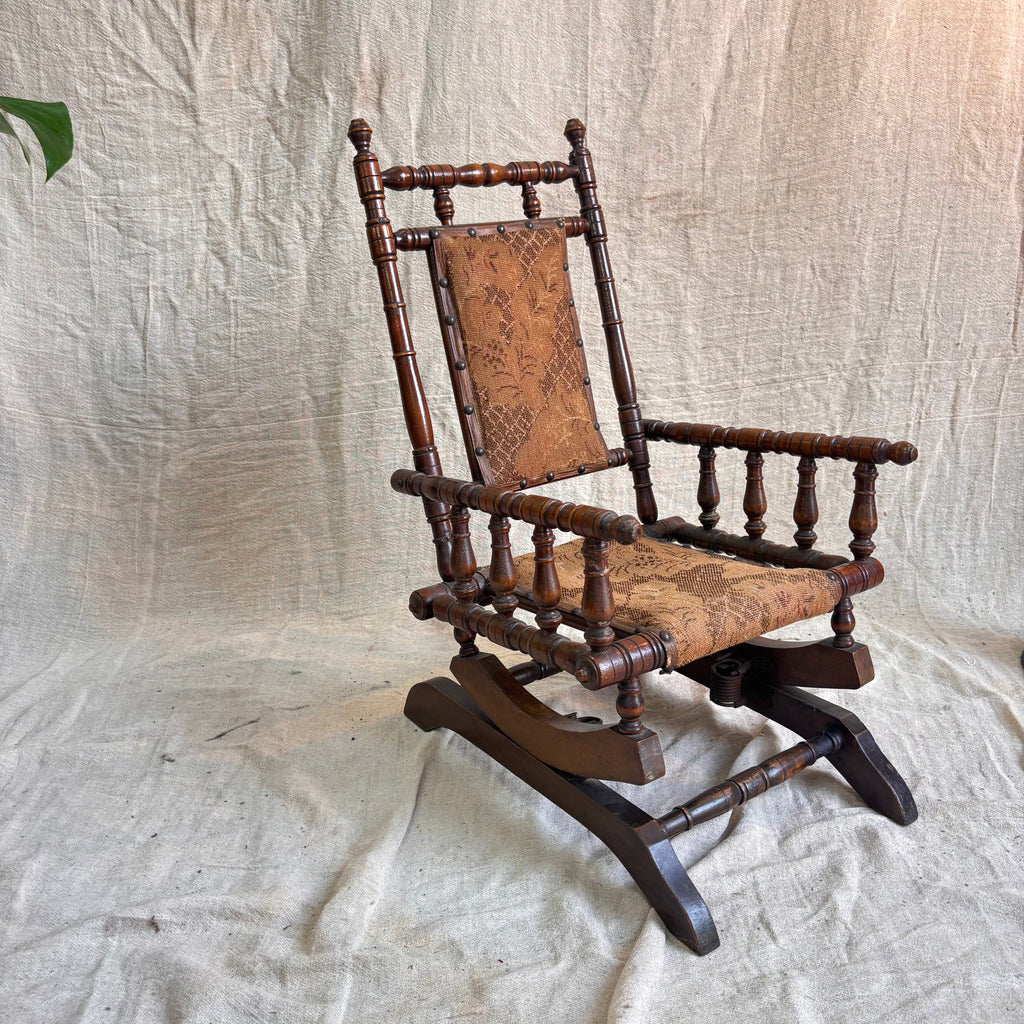 Vintage wooden rocking chair with patterned seat on a textured fabric background