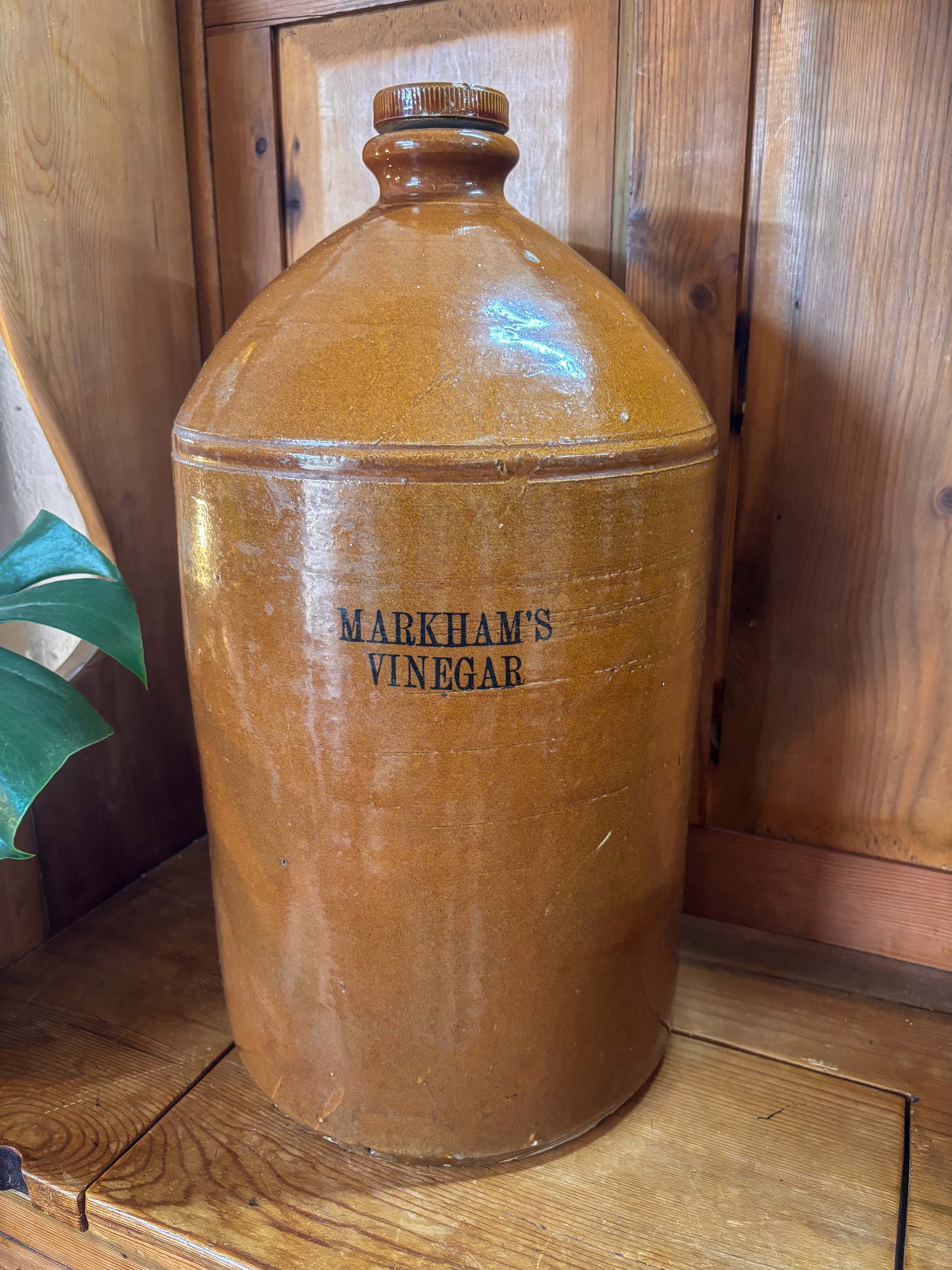 Large brown ceramic jar labeled 'Markham's Vinegar' on a wooden surface.