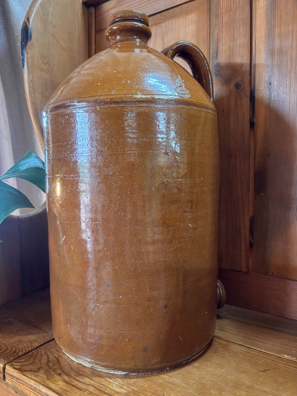 Vintage brown ceramic jar on a wooden surface with a wooden cabinet in the background.