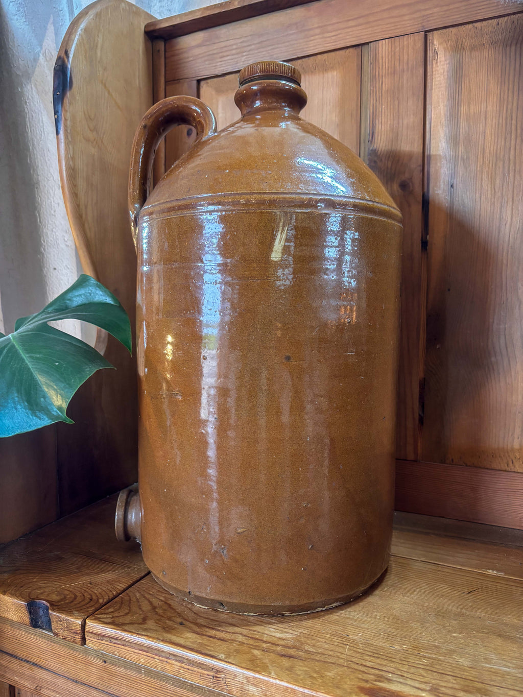 Brown ceramic jar on a wooden surface with a wooden cabinet in the background