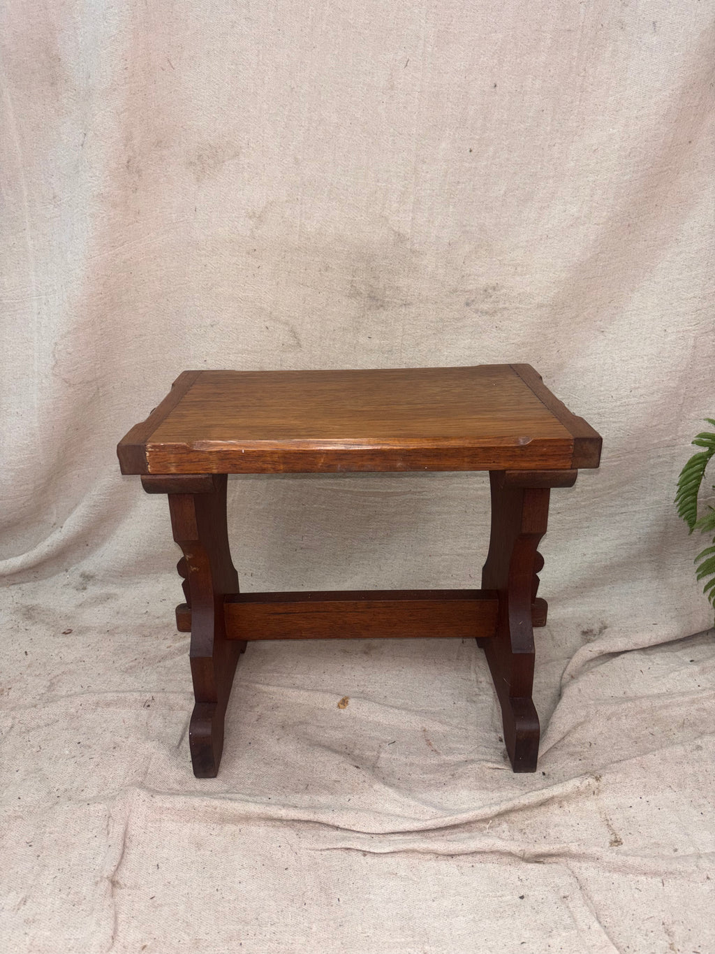 A wooden stool with a worn finish on a cream background. 