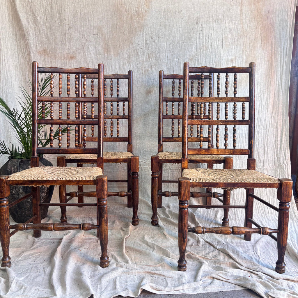 Set of four wooden chairs with rush seats on a textured white background