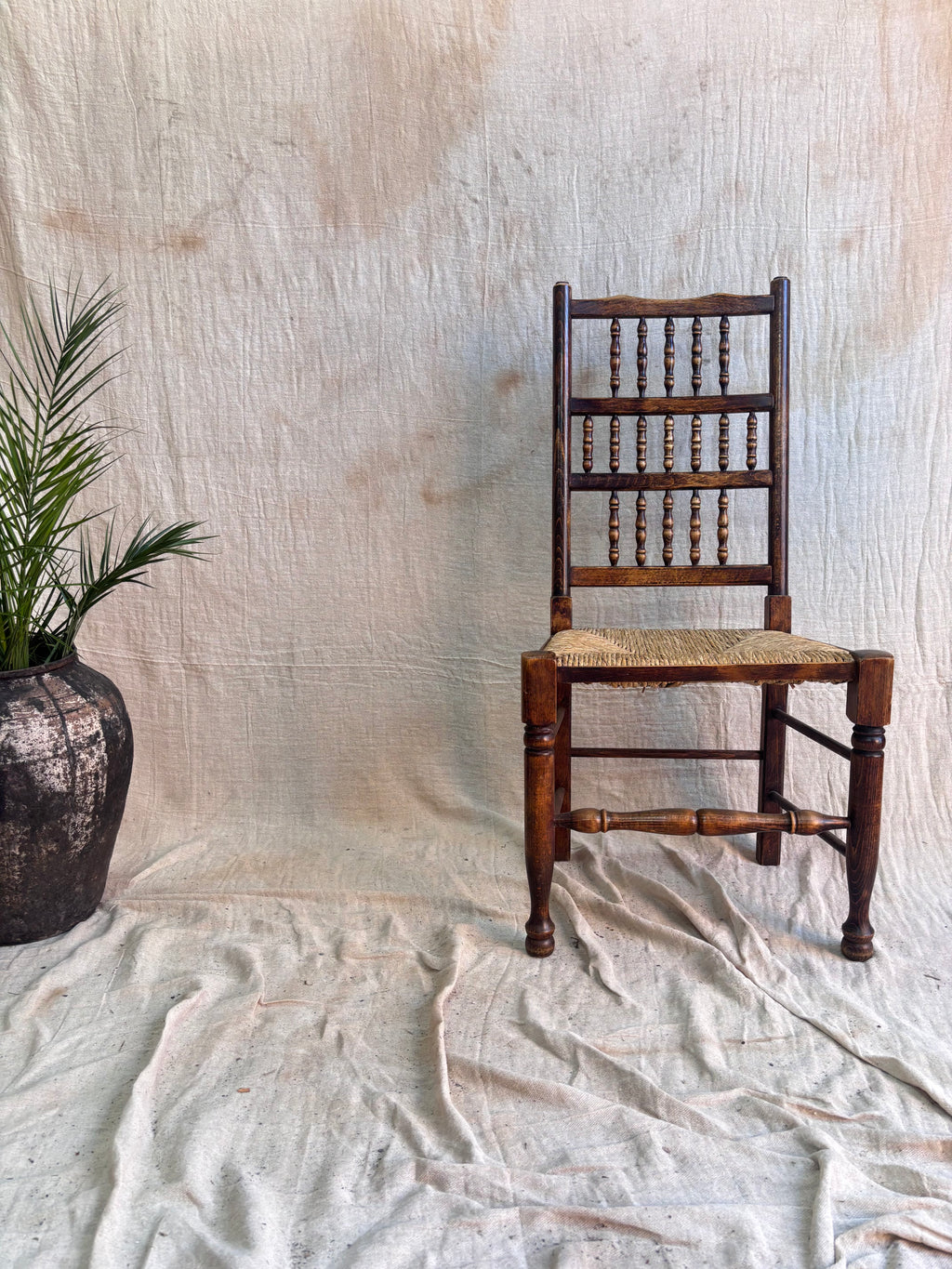Wooden chair with rush seat against a textured beige wall.