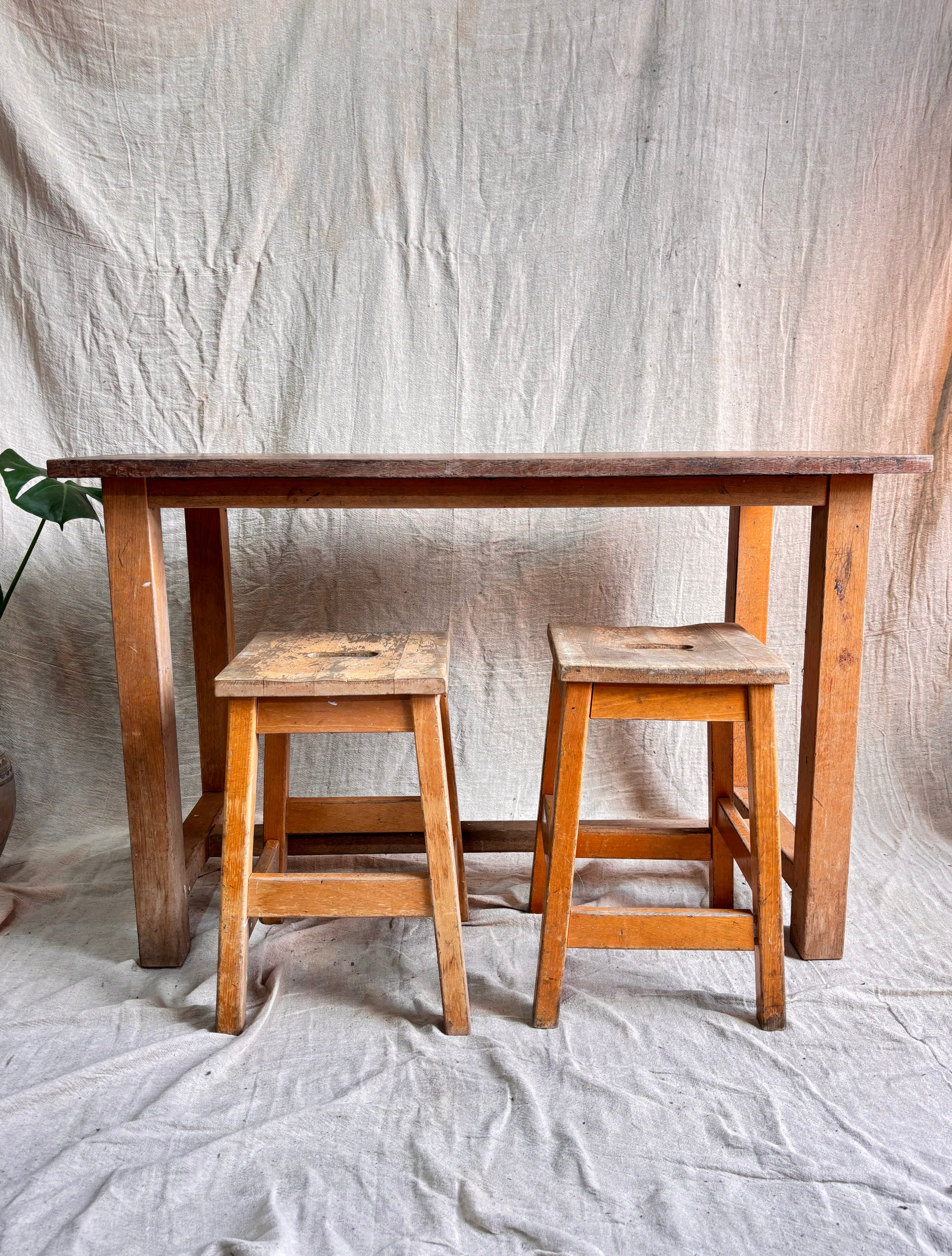 Wooden table with two stools against a plain background