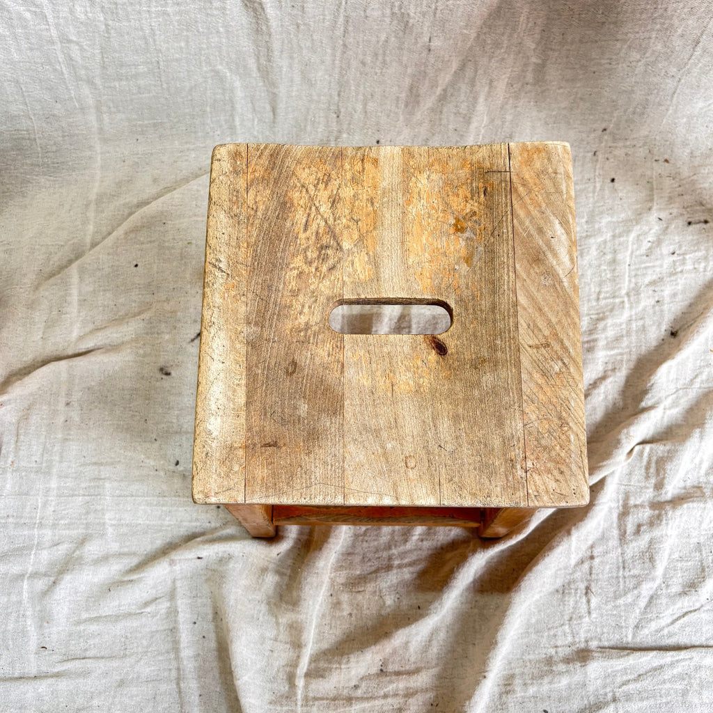 Wooden stool with a handle on a textured beige fabric background