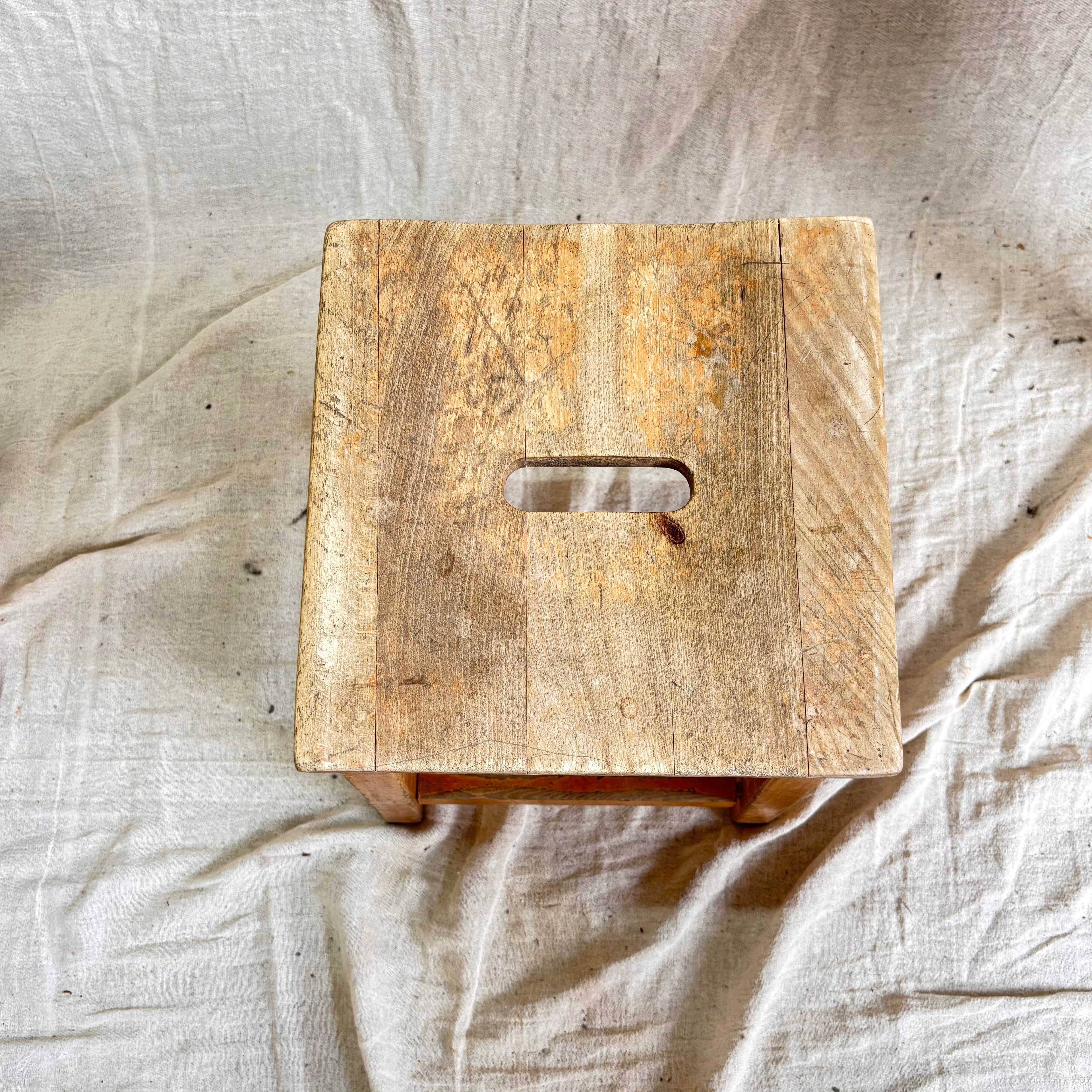 Wooden stool with a handle on a textured beige fabric background