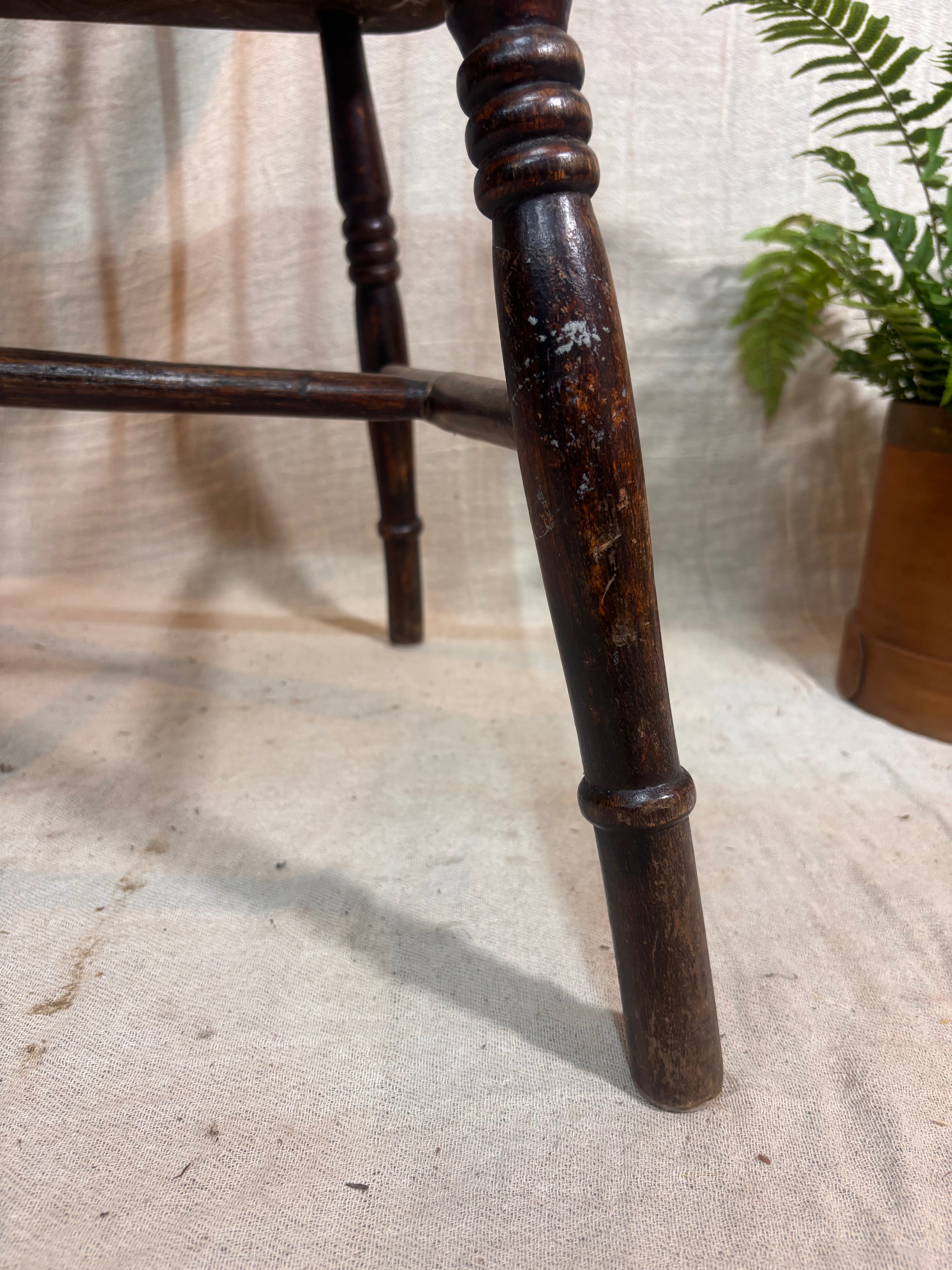 Close-up of a wooden chair leg on a textured surface with a plant in the background