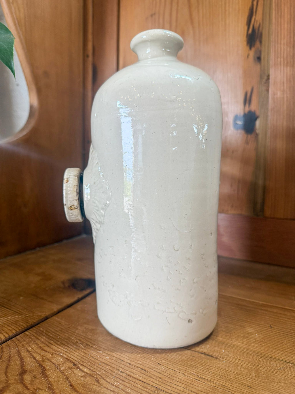 Stoneware hot water bottle on a wooden surface with a wooden cabinet in the background