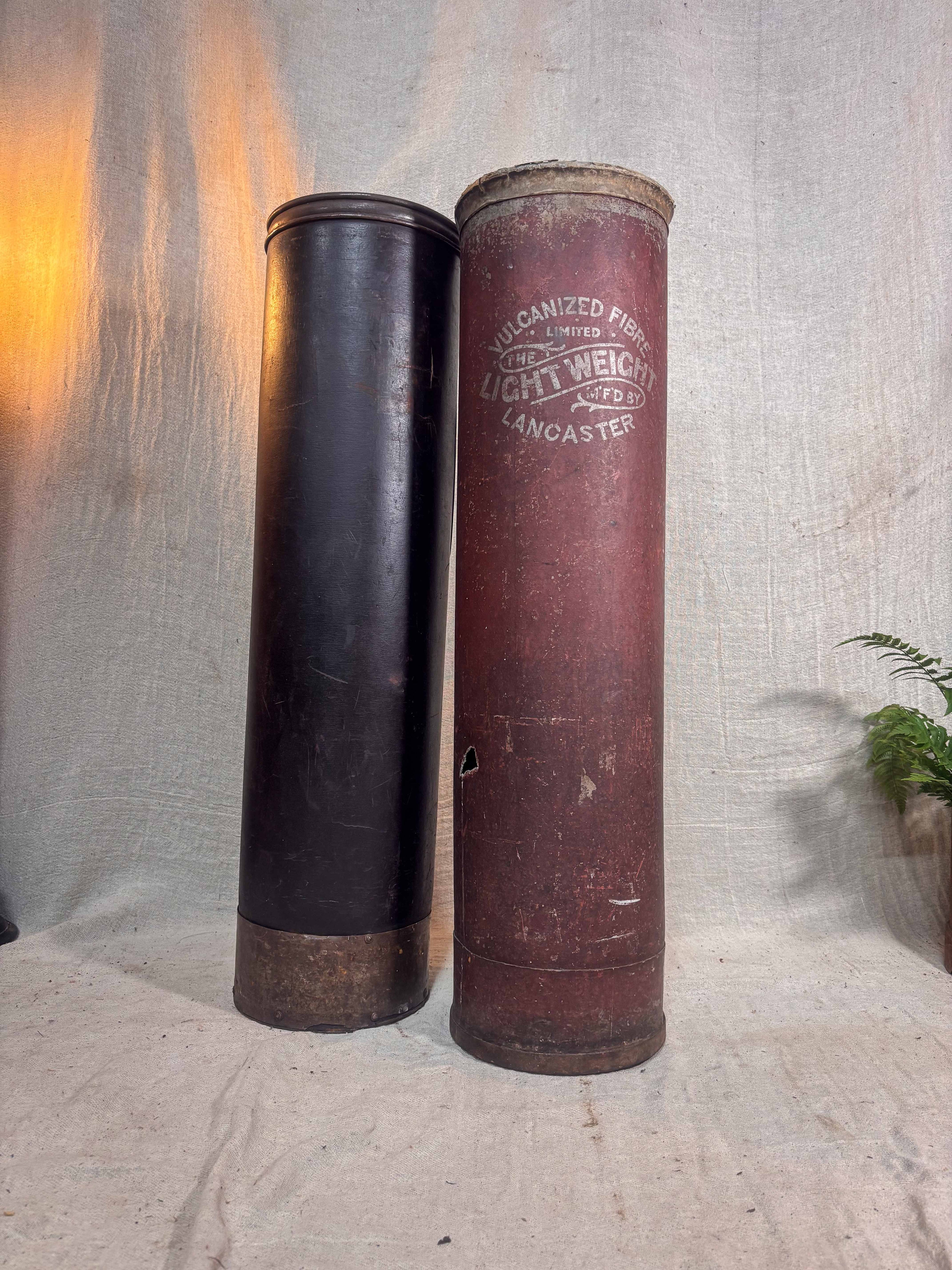 Two cylindrical cases, one black and one brown with text, against a textured gray background.