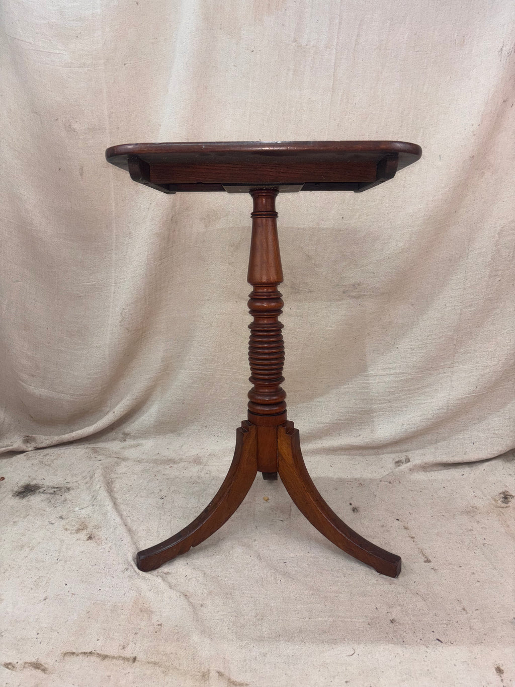 Wooden side table with a single pedestal leg on a plain background