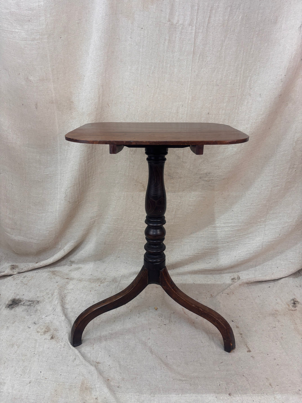 Wooden table with a single leg on a textured white background
