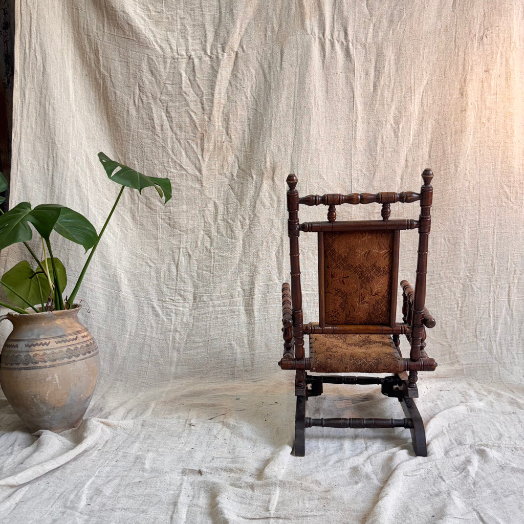 Vintage wooden rocking chair with a plant on a textured white background