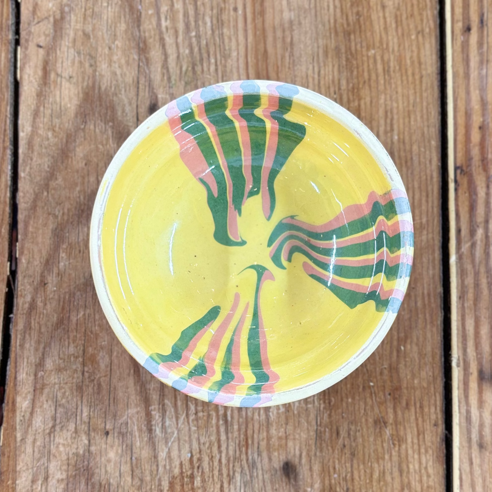 Round yellow bowl with colourful design on a wooden surface